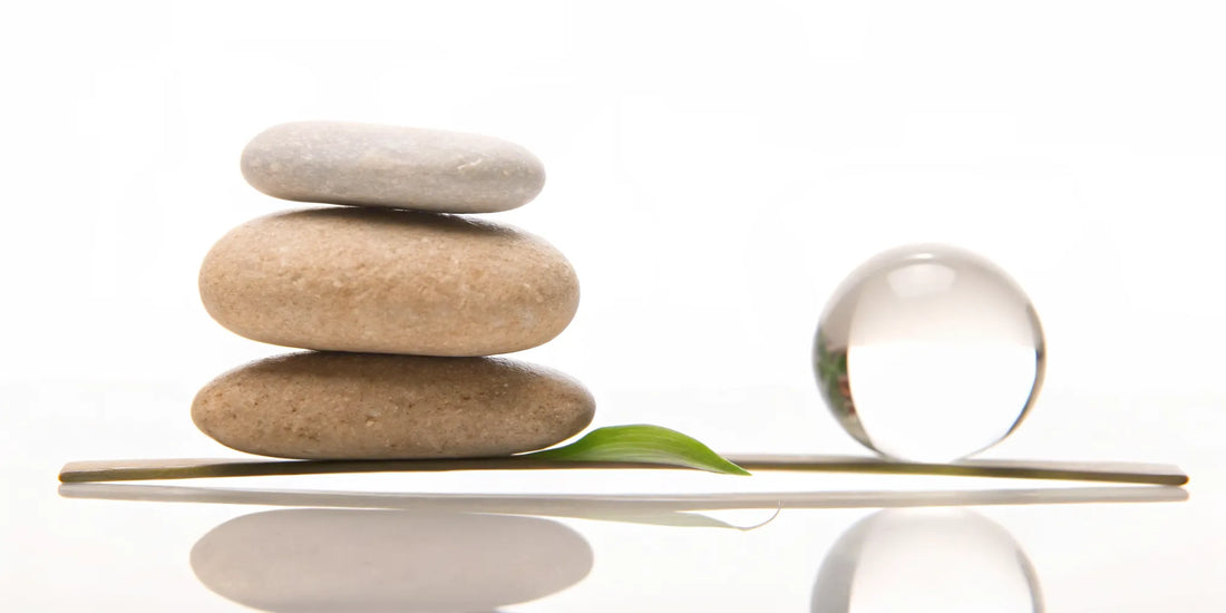 Balanced stones and a glass sphere on a leaf for achieving mood balance and overall wellness.