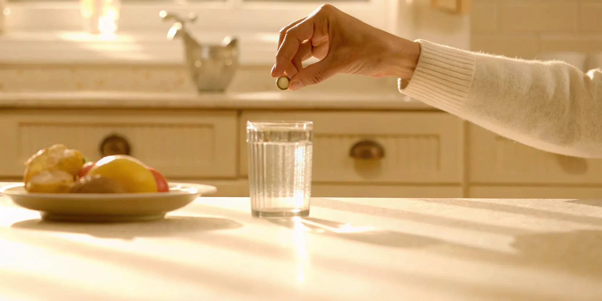 Person taking a postbiotic supplement in a sunlit kitchen with a glass of water and healthy breakfast