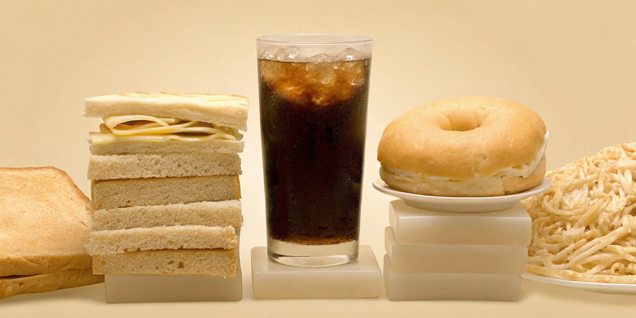A collection of the 7 worst foods for gut health, including a sandwich, bagel, pasta, and soda.