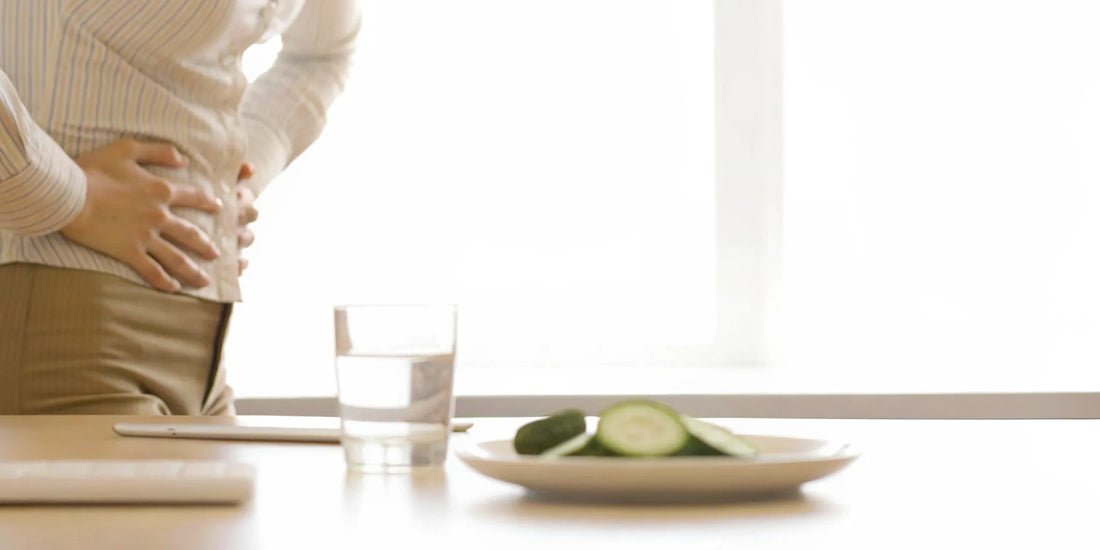 A person with water bloating holding their stomach in discomfort next to a glass of water.