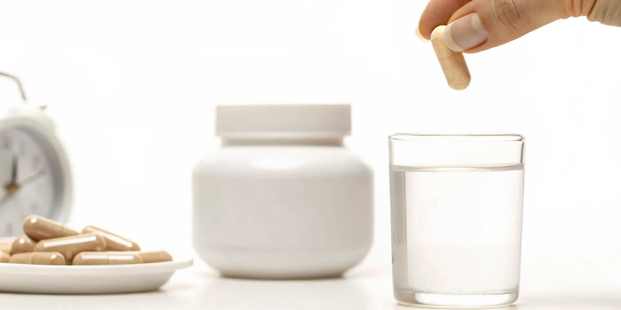 A person about to take a postbiotic supplement capsule with a glass of water.