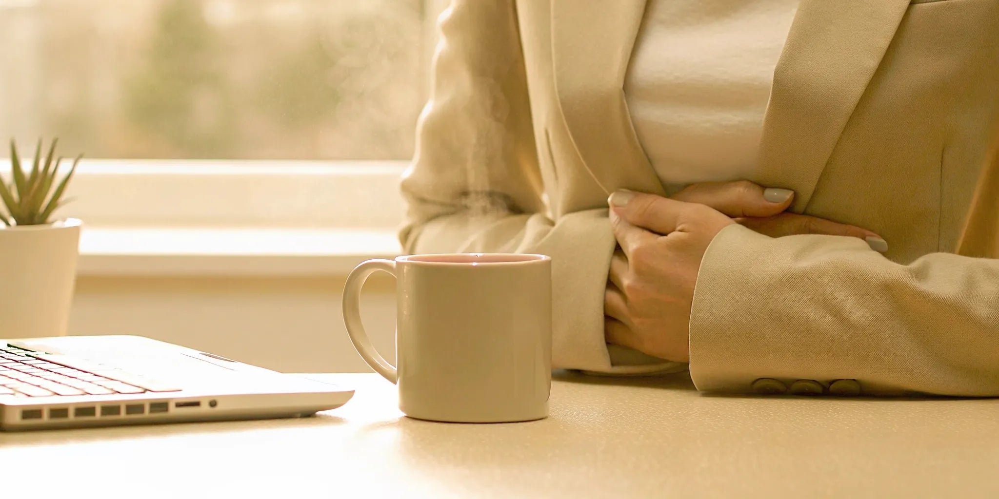 Woman holding her stomach at her desk, experiencing the anxiety indigestion gives.