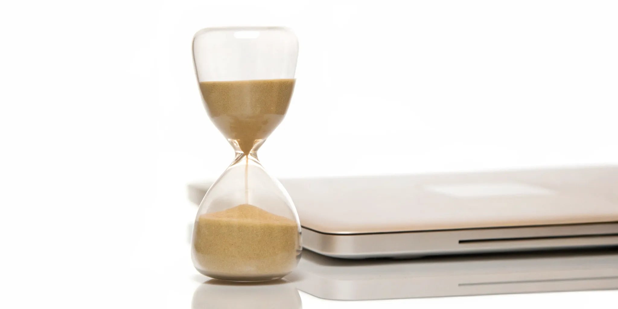 Hourglass and closed laptop for mood balance and time management for busy professionals.