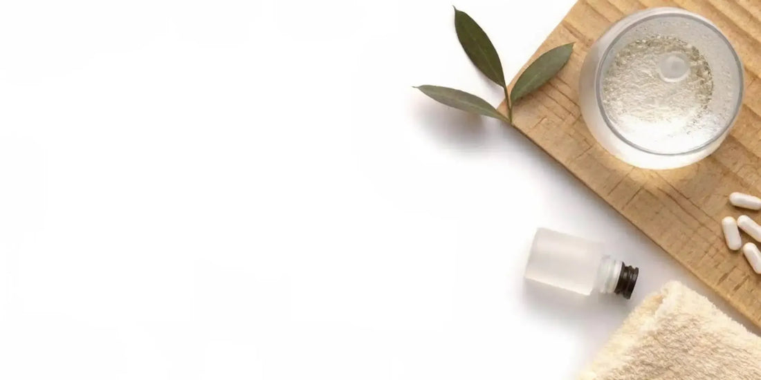 A top-down view of a minimalist wellness supplement setup with a water glass and green leaf in warm natural morning sunlight
