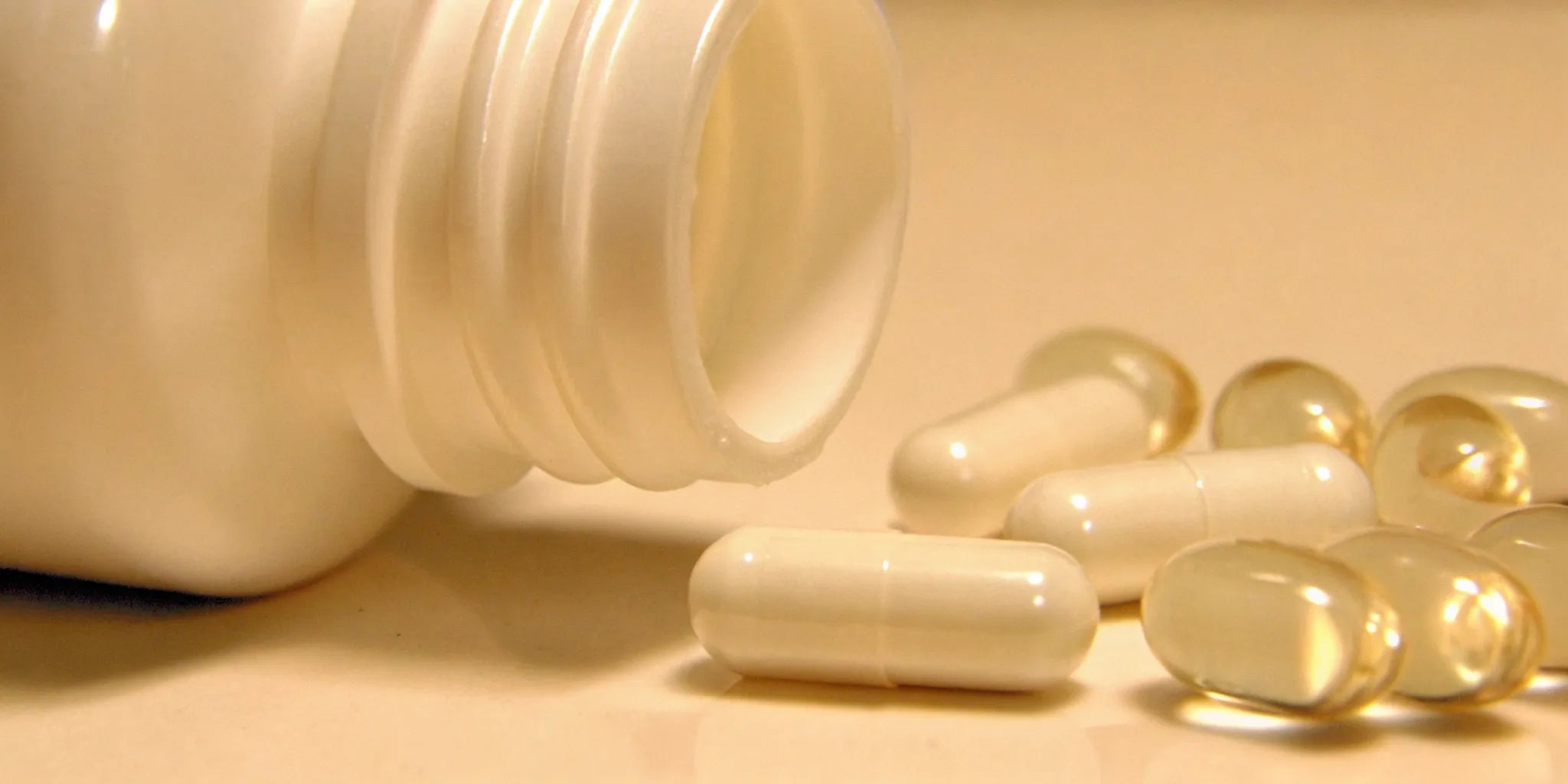 Postbiotics supplements in white capsules spilled out of a bottle.
