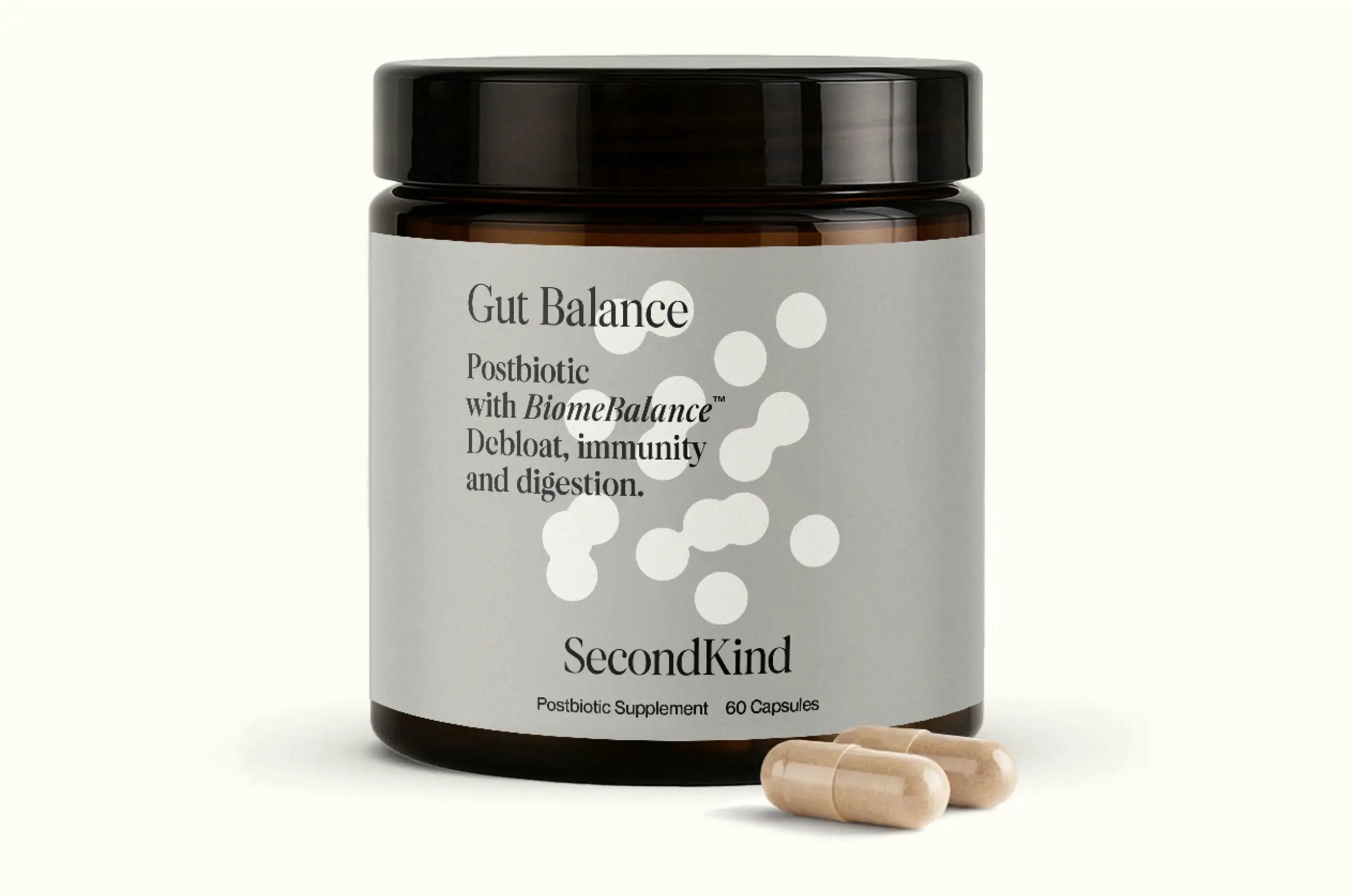 A brown jar labeled “Gut Balance” by SecondKind, described as a postbiotic supplement for debloating, immunity, and digestion, with two beige capsules placed in front of the jar.
