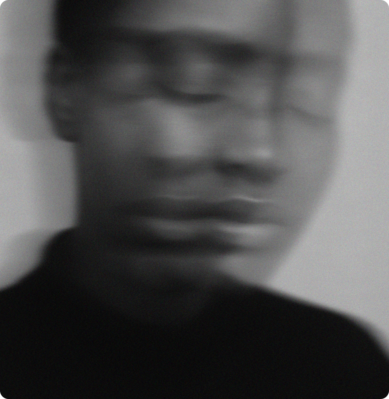 A black and white, blurred portrait of a persons face with eyes closed, creating a dreamy and abstract effect. The image conveys a sense of calm or introspection.