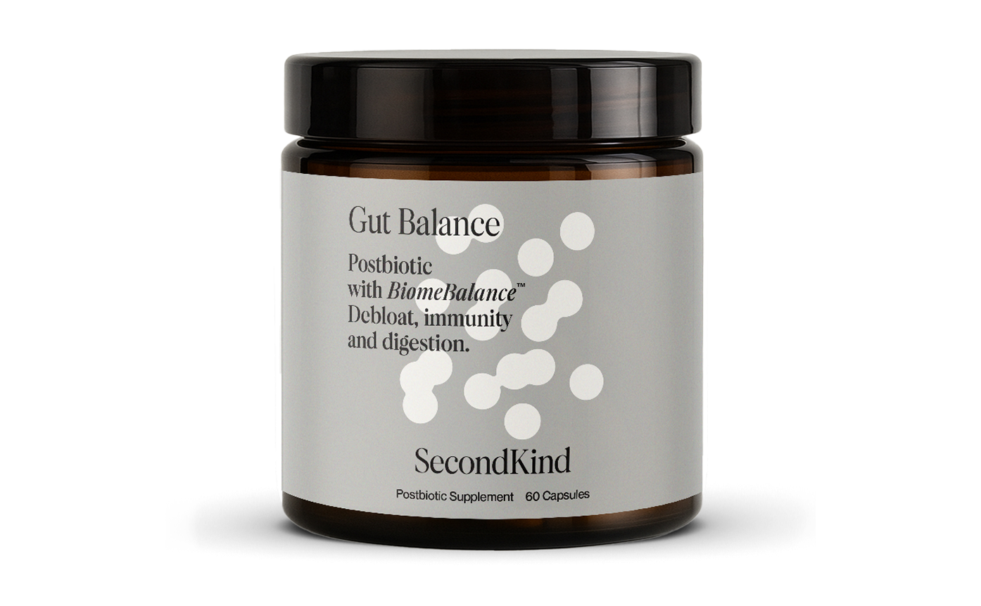 A brown jar labeled Gut Balance by SecondKind, described as a postbiotic supplement with BiomeBalance for debloat, immunity, and digestion. The label is white with minimalistic design and abstract circular patterns.
