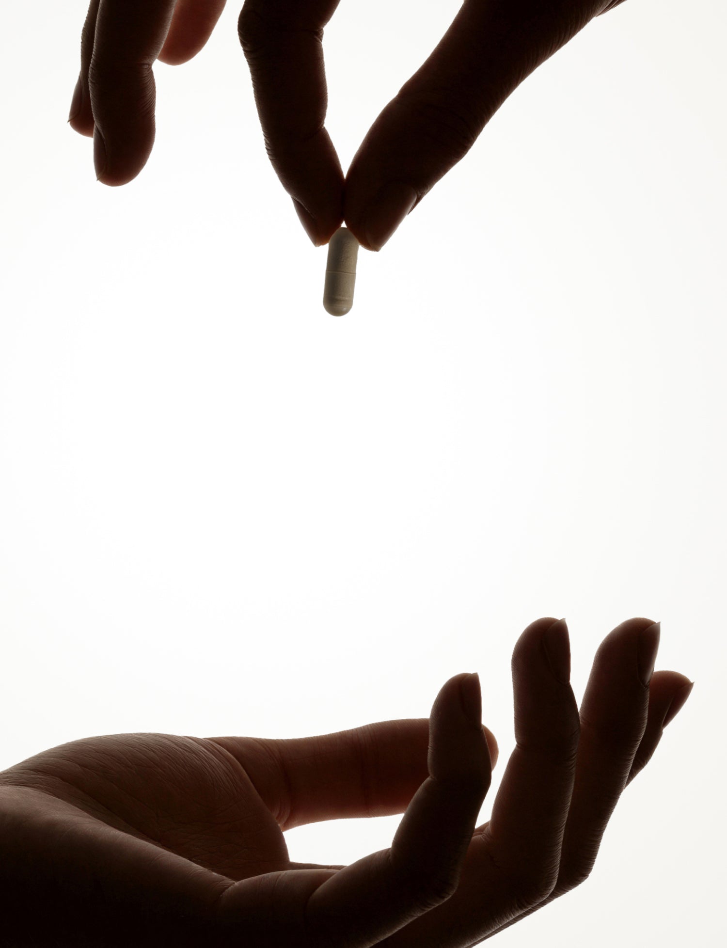 A silhouetted hand holds a capsule above another open hand, as if about to pass or receive the pill, against a white background.