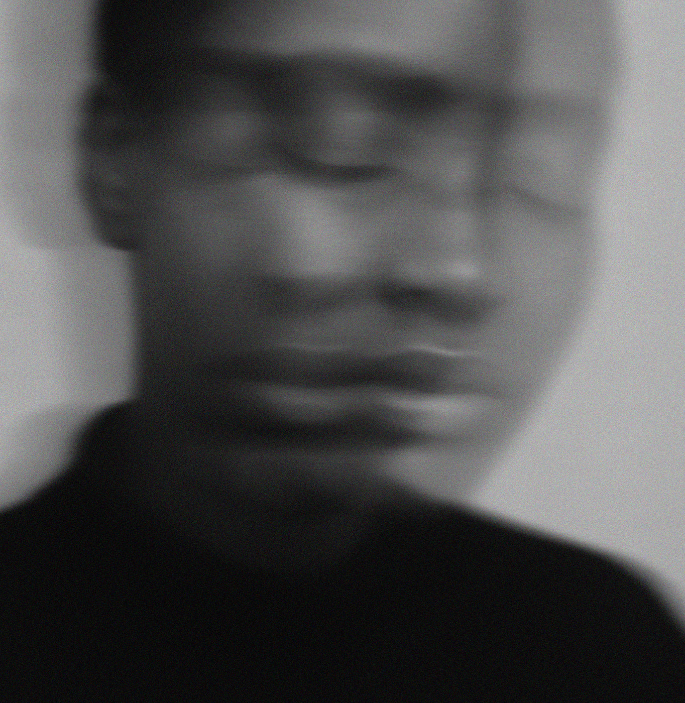 A blurred, black and white close-up of a persons face with indistinct features and soft focus, conveying a sense of motion or emotional ambiguity.